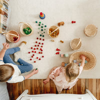 Children play with colourful loose parts and woven bamboo baskets in a bright room including an Olli Ella Kids Rattan basket for imaginative play