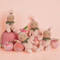 Four Dinky Dinkums peach themed dolls sit among pink peaches and a woven basket against a soft peach background