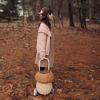 Child pulling a two tone natural rattan mushroom luggy through a woodland setting with Olli Ella playful design for imaginative outdoor adventures