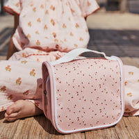 Olli Ella Kids pink floral See Ya wash bag with a handy carry handle resting on a child lap for travel days and overnight stays