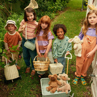 Five children enjoy imaginative outdoor play with woven baskets teddy bears and a pale wheeled luggy from Olli Ella Kids Rattan